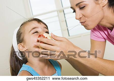Stock Image - Side profile of a mother feeding her daughter. Fotosearch