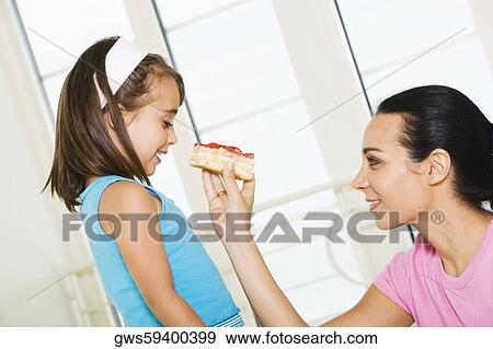 Stock Photo - Side profile of a mother feeding her daughter. Fotosearch