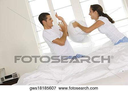 Stock Photo - Side profile of a young couple having a pillow fight. Fotosearch