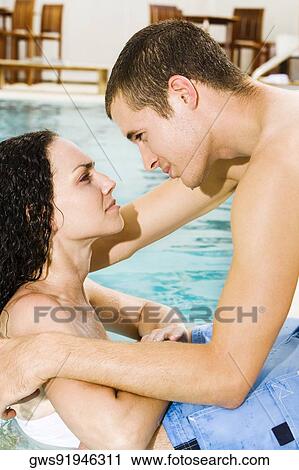 Stock Image - Side profile of a young couple in a swimming pool. Fotosearch