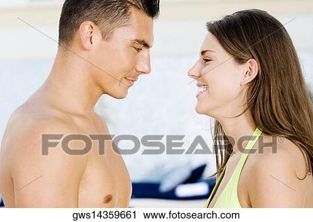 Stock Image - Side profile of a young couple looking at each other at the poolside. Fotosearch