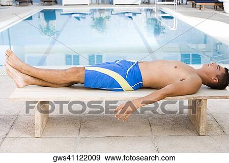 Side profile of a young man lying on a bench at the poolside View Large Photo Image Stock Photo - Side profile of a young man lying on a bench at the poolside. Fotosearch