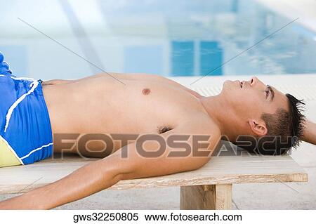 Side profile of a young man lying on a bench at the poolside View Large Photo Image Stock Photography - Side profile of a young man lying on a bench at the poolside. Fotosearch