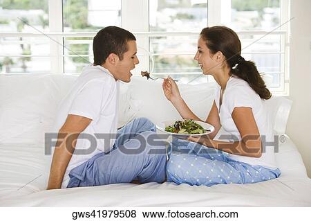 Stock Photo - Side profile of a young woman feeding a young man salad. Fotosearch
