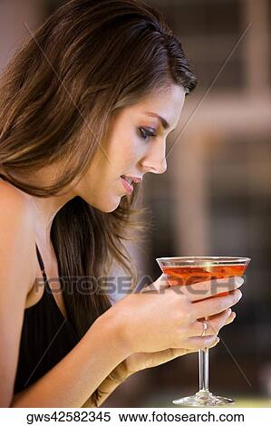 Stock Photography - Side profile of a young woman holding a glass of martini. Fotosearch