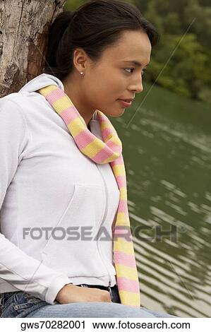 Side profile of a young woman leaning against a tree View Large Photo Image Stock Image - Side profile of a young woman leaning against a tree. Fotosearch