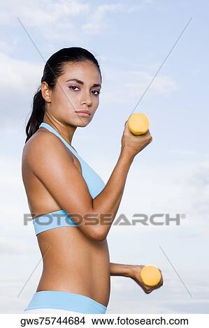 Side profile of a young woman exercising with dumbbells View Large Photo Image Picture - Side profile of a young woman exercising with dumbbells. Fotosearch