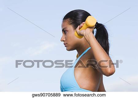 Stock Photo - Side profile of a young woman exercising with dumbbells. Fotosearch