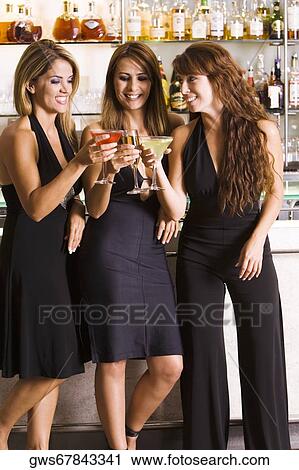 Three women holding glasses at a bar View Large Photo Image Stock Image - Three women holding glasses at a bar. Fotosearch