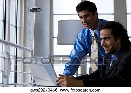 Two businessmen working on a laptop View Large Photo Image Stock Photograph - Two businessmen working on a laptop. Fotosearch