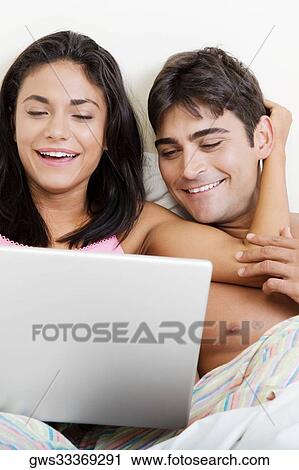 Young couple using a laptop on a bed View Large Photo Image Stock Image - Young couple using a laptop on a bed. Fotosearch