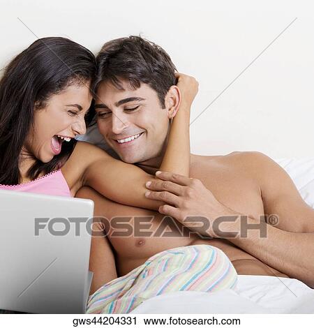 Young couple using a laptop on a bed View Large Photo Image Stock Image - Young couple using a laptop on a bed. Fotosearch
