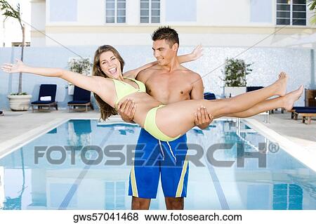 Stock Photo - Young man carrying a young woman at the poolside. Fotosearch