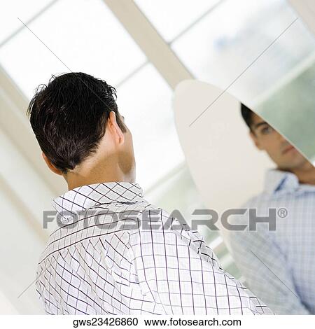 Stock Image - Young man looking at himself in a mirror. Fotosearch