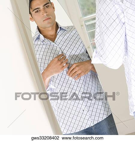 Young man looking at himself in a mirror View Large Photo Image Stock Image - Young man looking at himself in a mirror. Fotosearch