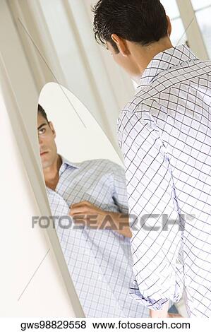 Young man looking at himself in a mirror View Large Photo Image Stock Photo - Young man looking at himself in a mirror. Fotosearch