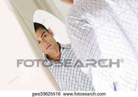Young man looking at himself in a mirror View Large Photo Image Stock Photograph - Young man looking at himself in a mirror. Fotosearch