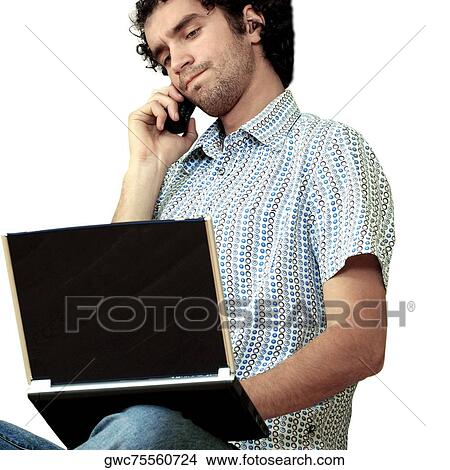 Picture - Young man talking on a mobile phone and using a laptop. Fotosearch