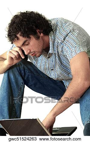 Stock Image - Young man talking on a mobile phone and using a laptop. Fotosearch