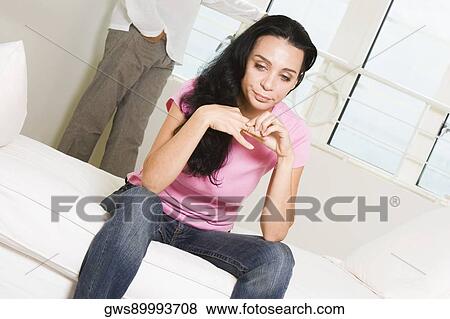 Young woman sitting on the bed with a young man standing behind her View Large Photo Image Stock Photo - Young woman sitting on the bed with a young man standing behind her. Fotosearch