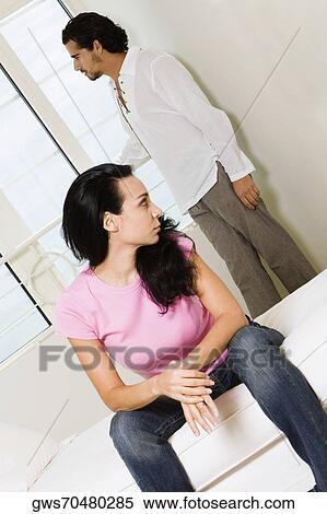 Young woman sitting on the bed with a young man standing behind her View Large Photo Image Stock Photography - Young woman sitting on the bed with a young man standing behind her. Fotosearch
