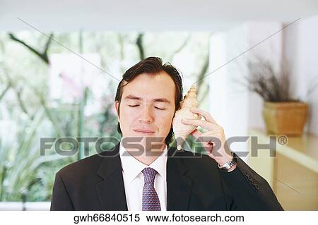 Close-up of a businessman holding a shell close to his ear View Large Photo Image Stock Photography - Close-up of a businessman holding a shell close to his ear. Fotosearch