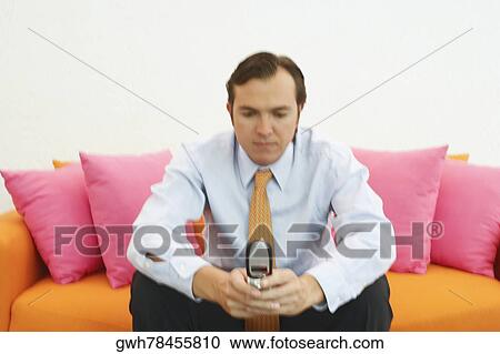 Close-up of a businessman sitting on a couch and using a mobile phone View Large Photo Image Stock Image - Close-up of a businessman sitting on a couch and using a mobile phone. Fotosearch