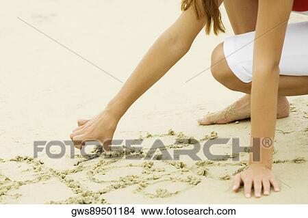 Picture - Close-up of a girl drawing in sand on the beach. Fotosearch
