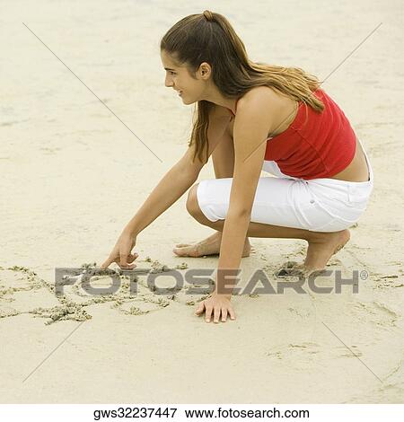 Stock Photo - Close-up of a girl drawing in sand on the beach. Fotosearch