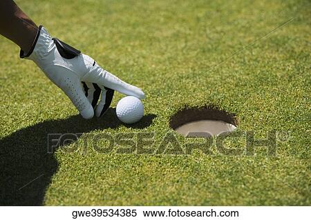 Stock Photography - Close-up of a man's hand putting a golf ball near a hole. Fotosearch