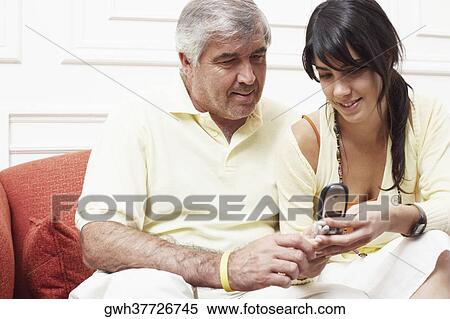 Close-up of a mature man sitting with his daughter on a couch and looking at a mobile phone View Large Photo Image Stock Photography - Close-up of a mature man sitting with his daughter on a couch and looking at a mobile phone. Fotosearch