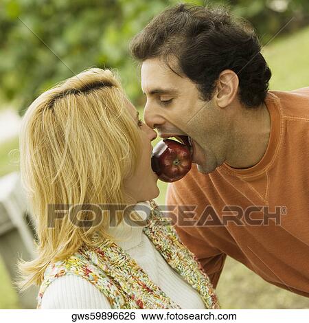 Close-up of a mid adult man and a young woman holding an apple between their teeth View Large Photo Image Stock Photograph - Close-up of a mid adult man and a young woman holding an apple between their teeth. Fotosearch