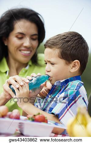 Stock Image - Close-up of a woman helping her son drink water from a bottle. Fotosearch