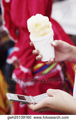 Stock Image - Close-up of a woman's hands holding an ice-cream and using a mobile phone. Fotosearch