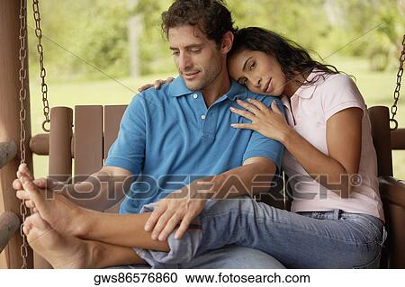 Stock Image - Close-up of a young couple sitting on a swing. Fotosearch