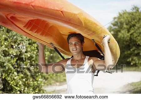 Stock Image - Close-up of a young man carrying a kayak on his head. Fotosearch