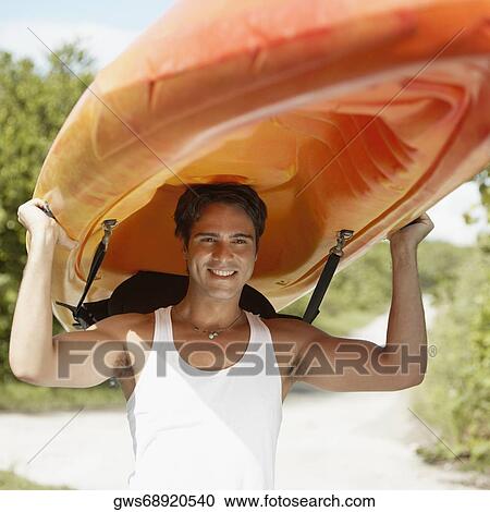 Stock Image - Close-up of a young man carrying a kayak on his head. Fotosearch