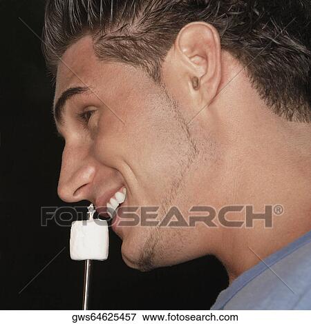Stock Photo - Close-up of a young man holding a marshmallow close to his mouth. Fotosearch