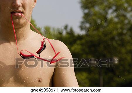 Stock Image - Close-up of a young man holding swimming goggles in his mouth. Fotosearch
