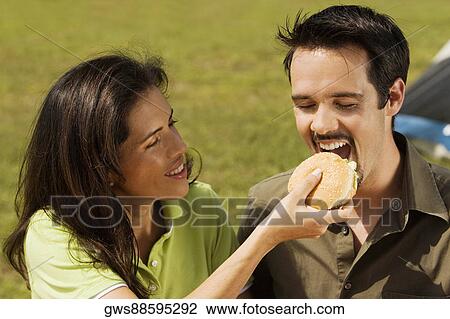 Stock Image - Close-up of a young woman feeding a burger to a young man. Fotosearch