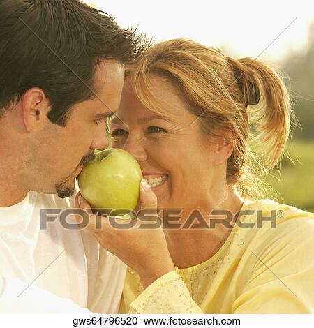 Close-up of a young woman holding an apple in front of a mature man View Large Photo Image Stock Image - Close-up of a young woman holding an apple in front of a mature man. Fotosearch