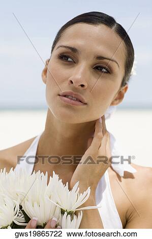 Stock Image - Close-up of a young woman holding flowers on the beach. Fotosearch