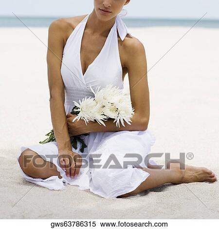 Close-up of a young woman sitting on the beach and holding flowers View Large Photo Image Stock Photography - Close-up of a young woman sitting on the beach and holding flowers. Fotosearch