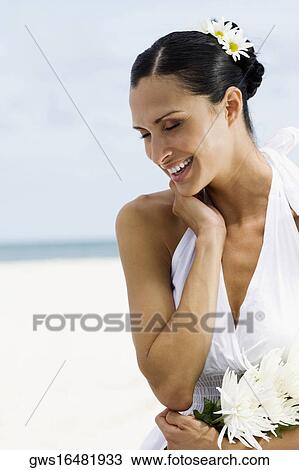 Stock Image - Close-up of a young woman smiling and holding flowers on the beach. Fotosearch