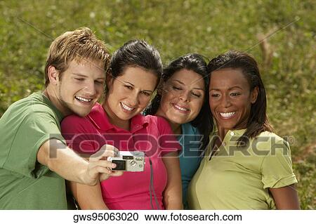 Stock Image - Close-up of three young women and a young man photographing themselves. Fotosearch