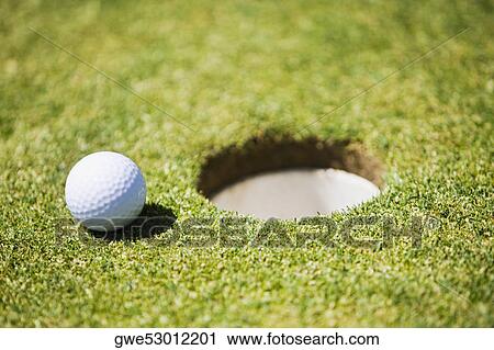 Stock Image - Golf ball at the edge of a hole. Fotosearch