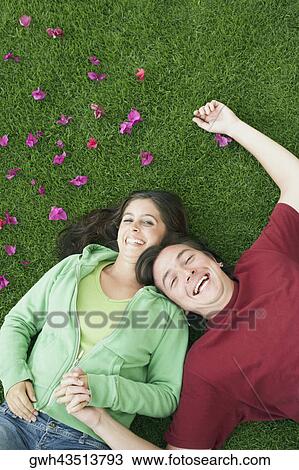 Stock Image - High angle view of a mid adult man and a young woman lying on the grass and laughing. Fotosearch