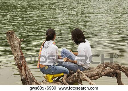 High angle view of a young couple sitting on a tree over a lake View Large Photo Image Stock Image - High angle view of a young couple sitting on a tree over a lake. Fotosearch