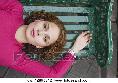 Stock Image - High angle view of a young woman lying on a bench. Fotosearch