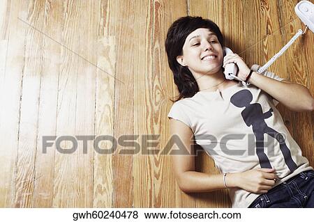 Stock Photo - High angle view of a young woman lying on the floor and talking on the telephone. Fotosearch